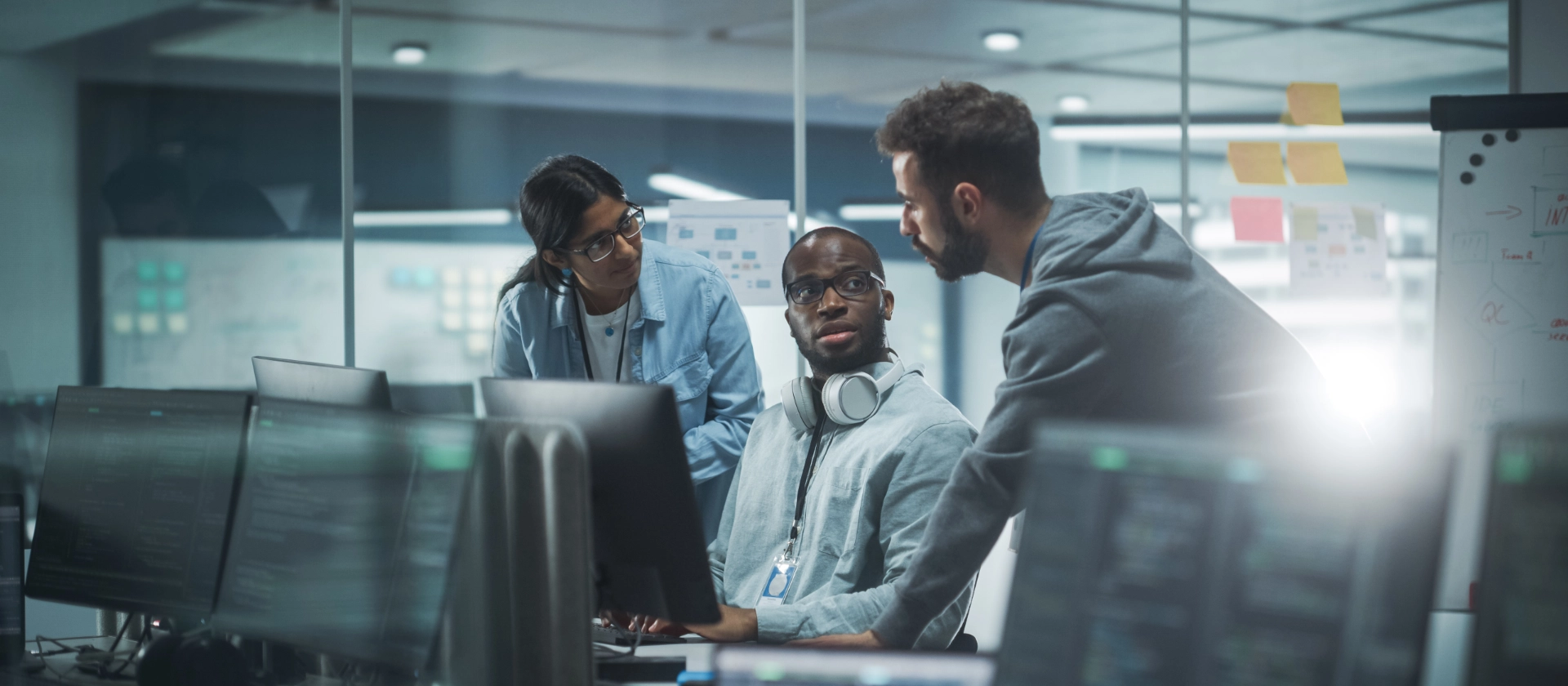 Drei Mitarbeitende aus dem Bereich msg Research beratschlagen sich am Arbeitsplatz neben ihren Computern