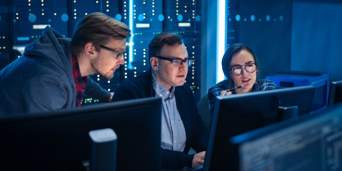 Zwei Kollegen und eine Kollegin aus dem Bereich Cyber Security sitzen konzentriert an einem Arbeitsplatz vor ihren Rechnern