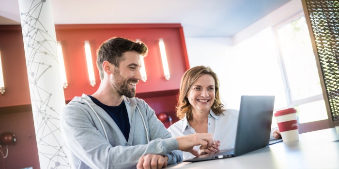 junger Entwickler zeigt erfahrener Kollegin Code am Laptop in der msg Service Lounge