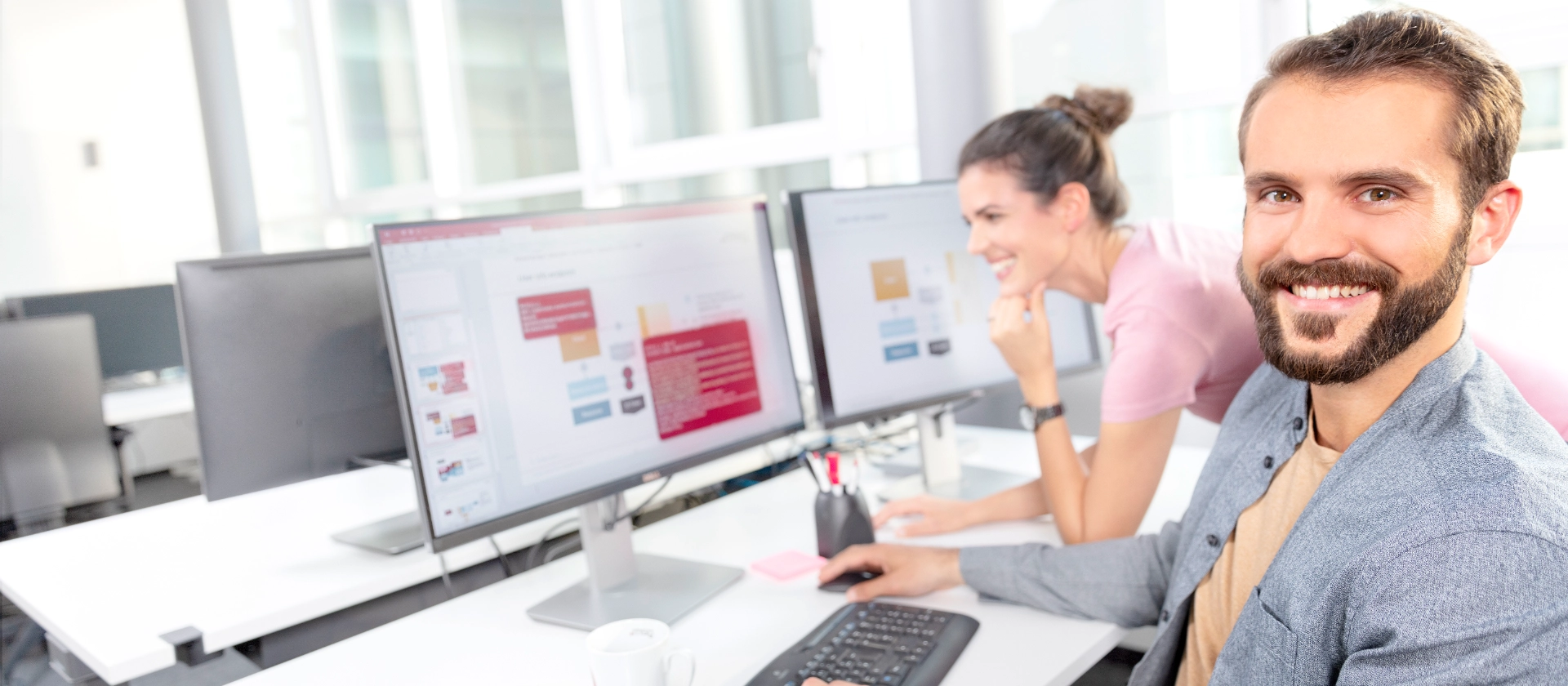 Zwei erfahrene Mitarbeitenden betrachten nebeneinander an ihren Arbeitsplätzen eine Powerpoint-Slide